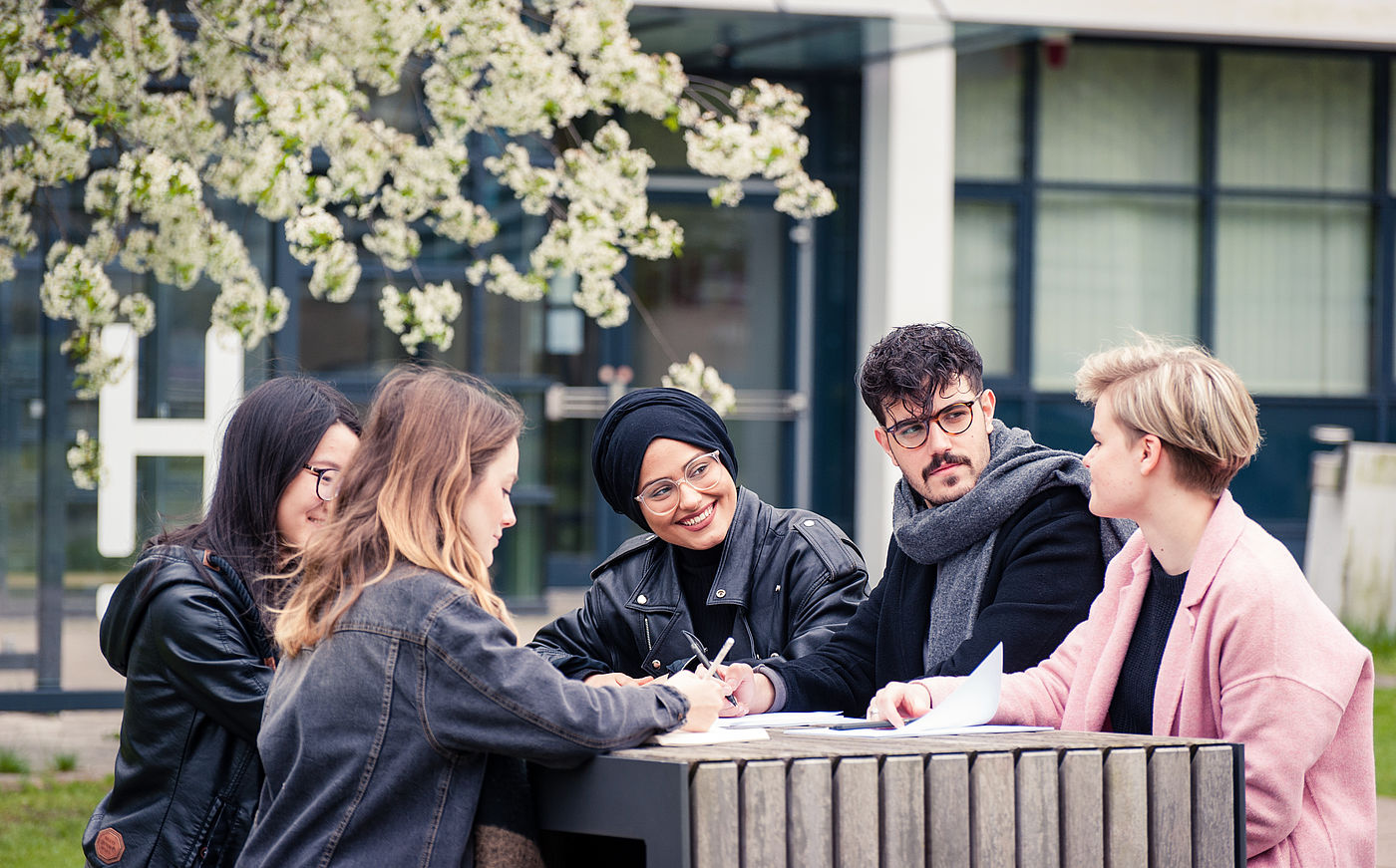 Studierende der HS Hannover sitzen vor dem Hochschulgebäude zusammen