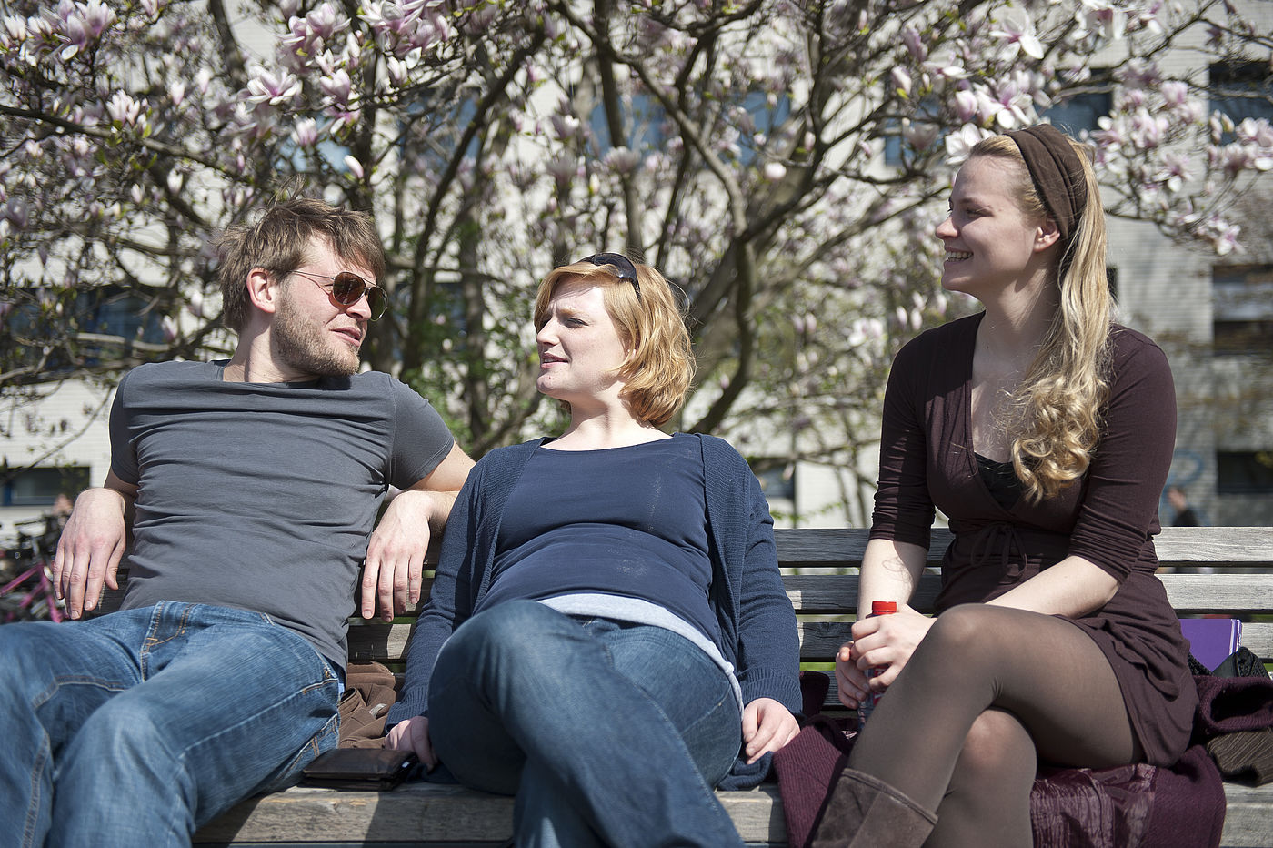 Studierende sitzen vorm Hochschulgebäude der HMTM Hannover unter Magnolienbäumen zusammen