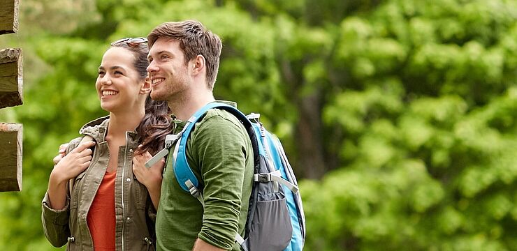 Zwei junge Menschen betrachten einen großen Wegweiser an einem Wanderweg im Grünen